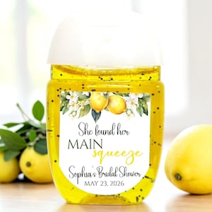 May include: A clear, rectangular hand sanitizer bottle with a white cap. The label features lemons, white flowers, and the text "She found her MAIN squeeze Sophia's Bridal Shower MAY 23, 2026."