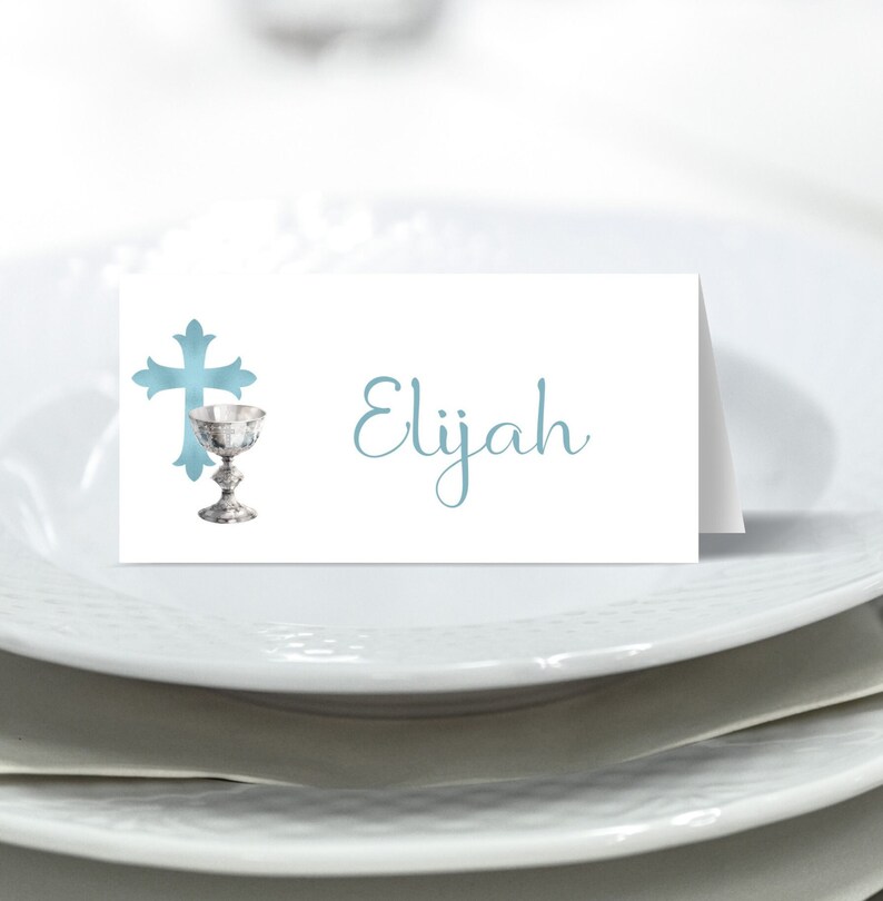 May include: A white place card with a blue cross and chalice design. The name Elijah is written in blue cursive script.