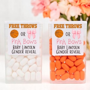Könnte beinhalten: Zwei durchsichtige Plastikbehälter gefüllt mit Süßigkeiten. Die Behälter haben Etiketten mit der Aufschrift "Free Throws or Pink Bows Baby Lincoln Gender Reveal". Ein Behälter enthält orangefarbene Süßigkeiten und der andere weiße Süßigkeiten.