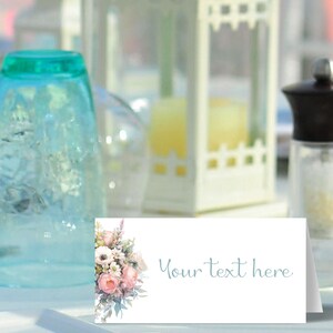 May include: A white place card with a floral design featuring pink and white flowers. The text "Your text here" is printed in blue on the right side of the card.