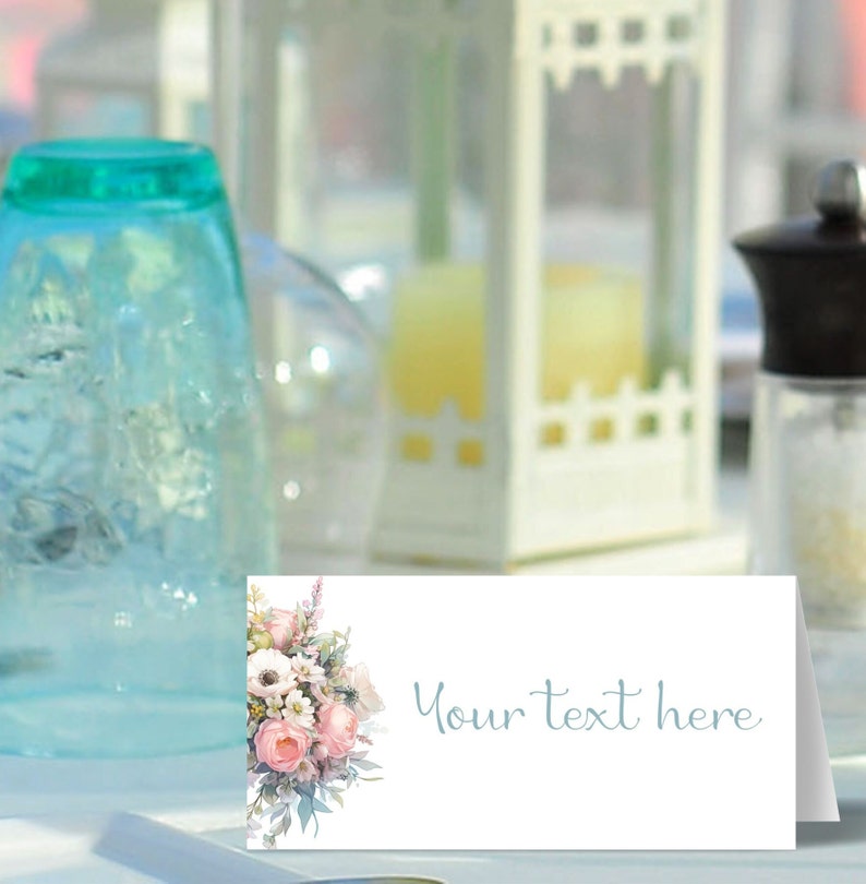 May include: A white place card with a floral design featuring pink and white flowers. The text "Your text here" is printed in blue on the right side of the card.