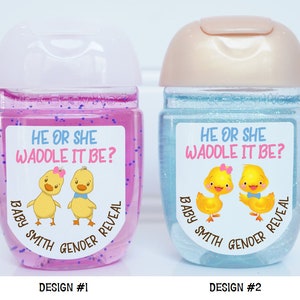 May include: Two clear plastic bottles with labels that say "He or She Waddle It Be?" and feature a cartoon image of a yellow duckling with a pink bow and a yellow duckling with a blue bow. The labels also say "Baby Smith Gender Reveal". The bottle on the left is pink and the bottle on the right is blue.