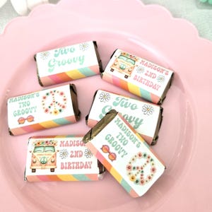 May include: Miniature candy bars with colorful wrappers. The wrappers feature the text "Two Groovy" and "Madison's 2nd Birthday" with daisy and peace sign graphics. The candy bars are arranged on a pink, scalloped plate.