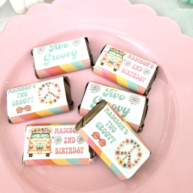 May include: Miniature candy bars with colorful wrappers. The wrappers feature the text "Two Groovy" and "Madison's 2nd Birthday" with daisy and peace sign graphics. The candy bars are arranged on a pink, scalloped plate.