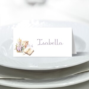 May include: White place card with a watercolor illustration of a candle, chalice, and bible. The text "Isabella" is printed in purple.