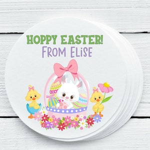 May include: Round sticker with a white bunny in a pink basket with colorful eggs. Two yellow chicks are on either side of the basket. The sticker says "Hoppy Easter! From Elise".