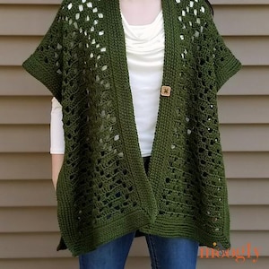 May include: A green crochet cardigan with a button closure. The open-front design features a textured stitch pattern and short sleeves. The cardigan is worn over a white top and blue jeans.