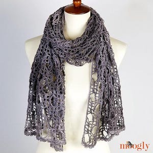 May include: A grey crochet scarf with a delicate lace pattern. The scarf is draped over a mannequin's neck and shoulders.