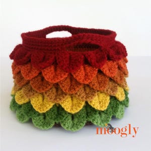 Può includere: Borsa all'uncinetto fatta a mano con un motivo a scaglie di drago. La borsa presenta una sfumatura di colori, che inizia con un rosso intenso nella parte superiore, passando per l'arancione e il giallo e terminando con il verde alla base. Ha due manici.