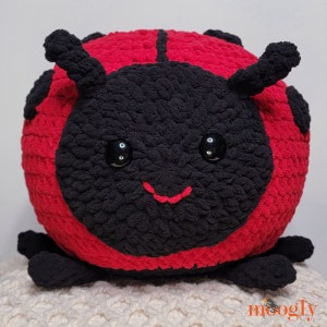 May include: A red and black crocheted ladybug plush toy with a smiling face and black eyes.