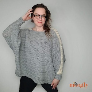 Può includere: Un maglione di uncinetto grigio con un bordo di uncinetto bianco sulle maniche. Il maglione ha una vestibilità ampia e un collo rotondo.