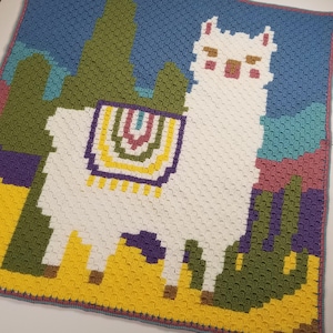 Puede incluir: Una llama blanca de crochet con una silla de montar colorida, rodeada de cactus de crochet verde, azul y rosa. La llama está de pie sobre un fondo de crochet amarillo.