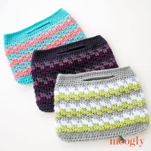 May include: Three handmade crochet bags in shades of blue, pink, purple, gray, white, and green. Each bag has a rectangular shape with a handle opening at the top. The bags are arranged diagonally, showcasing their textured stitch patterns.