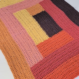 May include: A handmade crochet blanket in a patchwork design. The blanket features a variety of warm colors, including shades of orange, pink, yellow, and brown. The textured stitches create a cozy and inviting look.