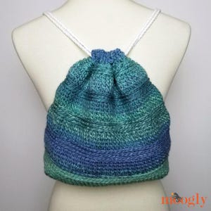 May include: A handmade drawstring backpack in shades of blue and green, with white rope straps. The knitted bag is displayed on a mannequin, showcasing its textured design and color gradient. The bag is a unique accessory.