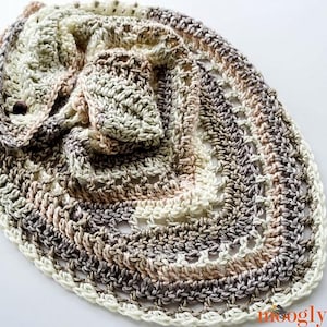 May include: A crocheted shawl in shades of beige, brown, and white with a lacy pattern. The shawl is folded in half and has a button on one side.