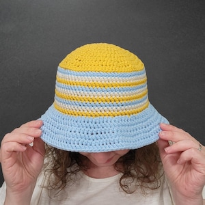 May include: A crocheted bucket hat with yellow and blue stripes. The hat is made of a soft, textured yarn.
