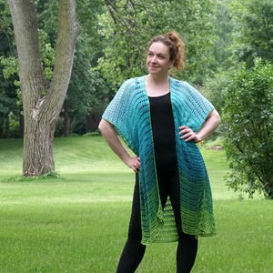 May include: A teal and green crochet cardigan with a long, open front. The cardigan is made with a lacy stitch and has a gradient of color from teal to green.