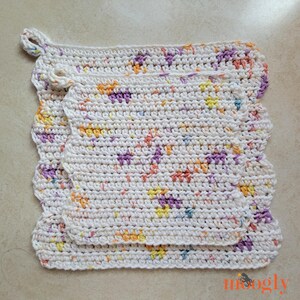 May include: Three crocheted potholders in a speckled pattern. The potholders are white with colourful flecks of purple, orange, yellow, and blue. The edges have a scalloped design. The top potholder has a loop for hanging.