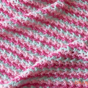 May include: Close-up of a handmade crochet blanket. The blanket features a diagonal striped pattern in shades of pink and light blue. The texture of the crochet stitches is visible, creating a soft and cozy appearance. The blanket is folded, showing its thickness.