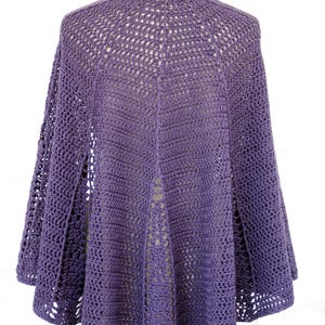 May include: A handmade, purple crochet cape with a unique openwork design. The cape features a round neckline and flared sleeves, showcasing a detailed, open stitch pattern. The back of the cape has a central seam and a flowing, open design.