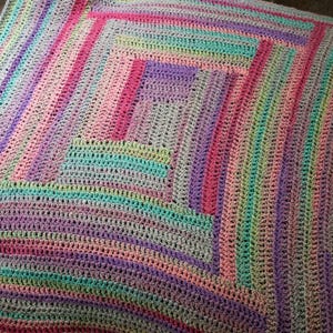 May include: A handmade, colorful crochet blanket with a geometric design. The blanket features a variety of pastel colors, including pink, purple, green, and yellow, arranged in stripes and squares. The texture of the crochet is visible, adding to the handmade aesthetic.