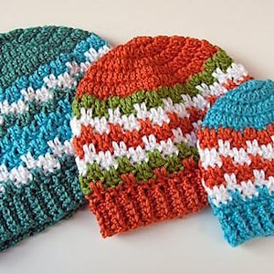 May include: Three colorful crochet beanies. One is teal, blue, and white. Another is orange, green, and white. The third is blue, orange, and white. The beanies are handmade and have a textured appearance.