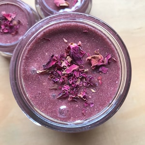 May include: A close-up of a glass jar filled with a purple-colored substance and topped with dried rose petals.
