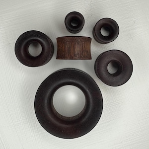 May include: A set of six wooden ear gauges in various sizes. The gauges are all dark brown and have a smooth, polished finish.