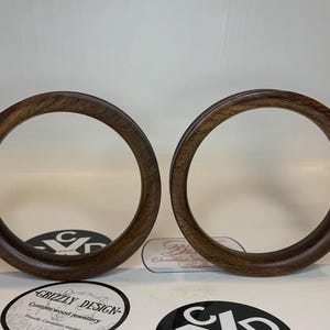 May include: Two dark brown wooden rings with a circular design. The rings are made of a rich, dark wood and have a smooth, polished finish. The rings are likely part of a jewelry set or craft project.