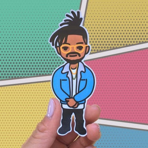 May include: A sticker featuring a cartoon illustration of a person with dark hair in a bun, wearing glasses, a blue jacket, and black pants. The background is a comic book style design with various colors.