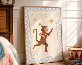 May include: A framed wall art print featuring a brown monkey wearing a blue party hat and a red and white striped collar. The monkey is reaching towards a yellow star against a cream background, surrounded by a blue and white checkered border.