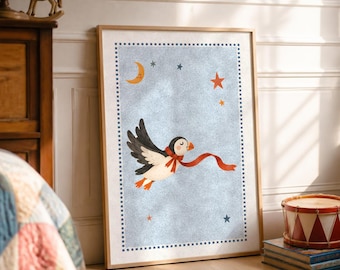 May include: A framed wall art print featuring a light blue background with a flying puffin wearing a red scarf. The illustration includes a yellow crescent moon, orange and blue stars, and a dark blue checkered border around the central image.
