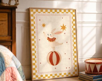 May include: A framed wall art print featuring a white rabbit with a red ruffled collar balancing on a red and white striped ball. The illustration is surrounded by a yellow and white chequered border and gold stars on a cream background.