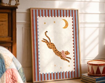 May include: A framed rectangular wall art print featuring a leaping leopard wearing a ruffled collar, set against a cream background with a yellow crescent moon and stars, bordered by a red and blue vertical striped frame design.