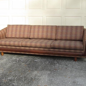 May include: A brown mid-century modern sofa with a geometric patterned fabric upholstery. The sofa has a wooden frame and legs.