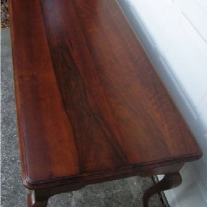 May include: A dark brown wooden coffee table with a smooth, polished surface and carved legs.