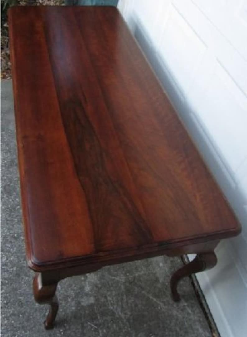 May include: A dark brown wooden coffee table with a smooth, polished surface and carved legs.