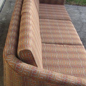 May include: A brown and beige patterned sofa with a curved back and armrests. The sofa has a geometric pattern with a mix of brown, beige, and white.