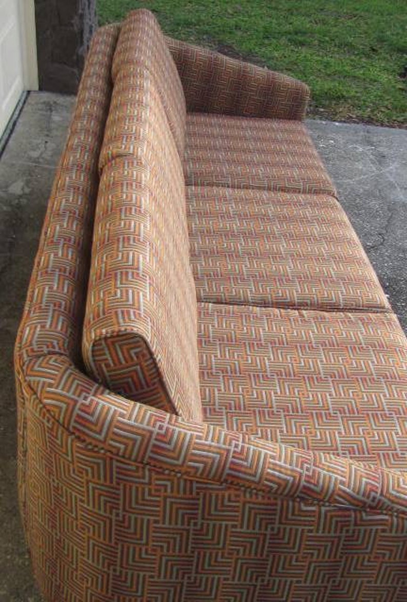 May include: A brown and beige patterned sofa with a curved back and armrests. The sofa has a geometric pattern with a mix of brown, beige, and white.