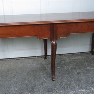 May include: A solid wood table with a rectangular top and four cabriole legs. The table is finished in a rich brown color.