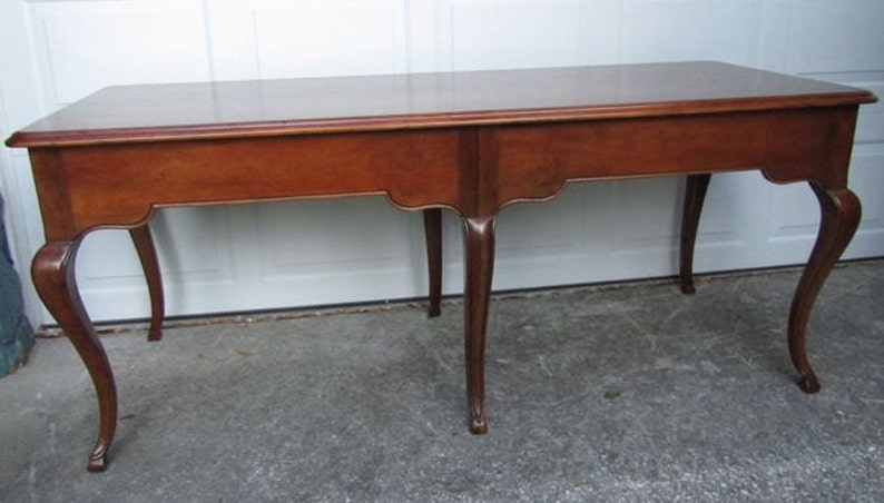 May include: A solid wood table with a rectangular top and four cabriole legs. The table is finished in a rich brown color.