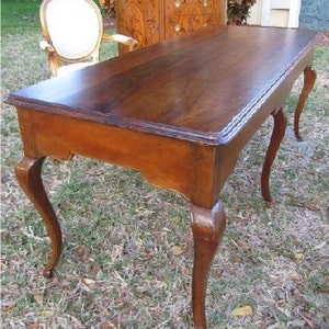 May include: A dark wood writing desk with a rectangular top and four cabriole legs. The desk has a simple design with a smooth finish.