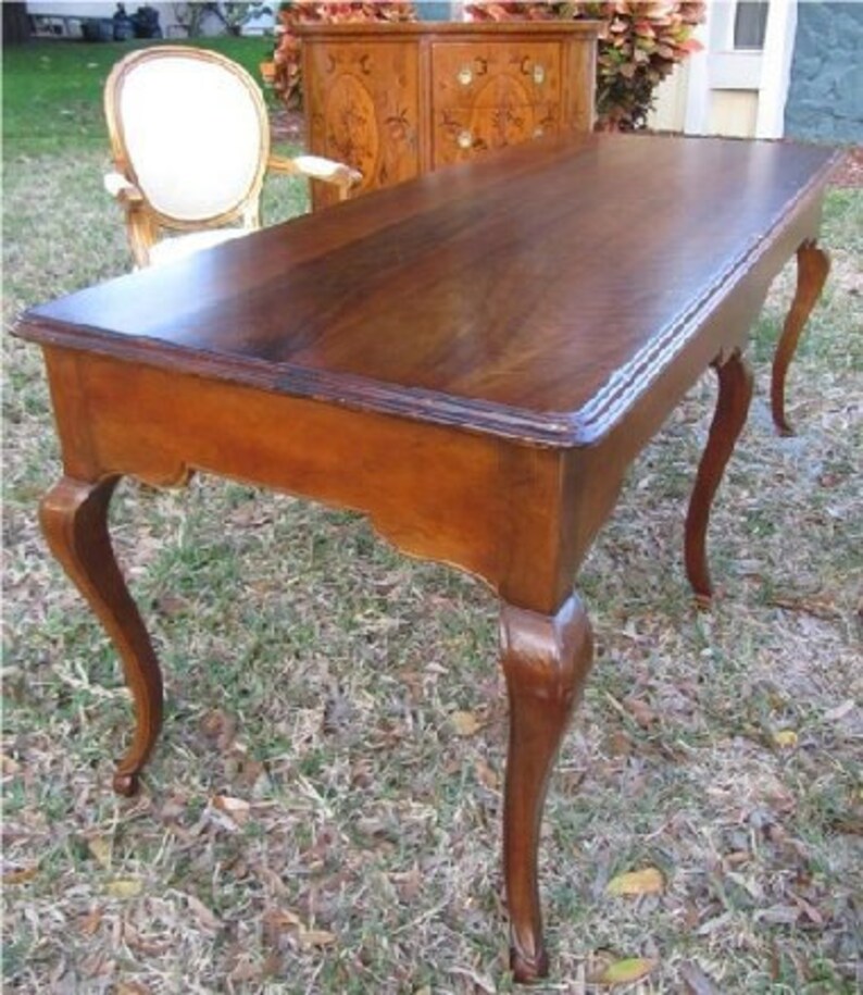 May include: A dark wood writing desk with a rectangular top and four cabriole legs. The desk has a simple design with a smooth finish.