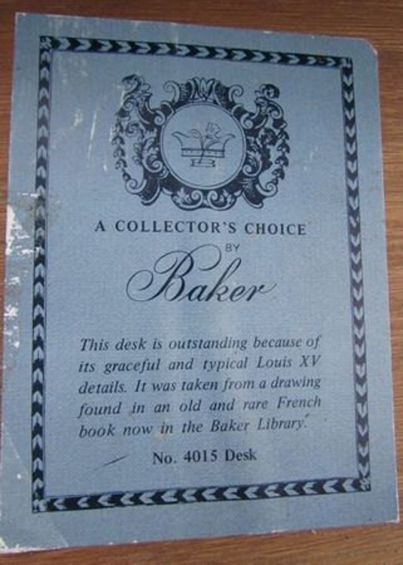 May include: A blue and white card with a decorative crest and the text "A Collector's Choice by Baker". The text below the crest reads "This desk is outstanding because of its graceful and typical Louis XV details. It was taken from a drawing found in an old and rare French book now in the Baker Library." The card also includes the text "No. 4015 Desk".