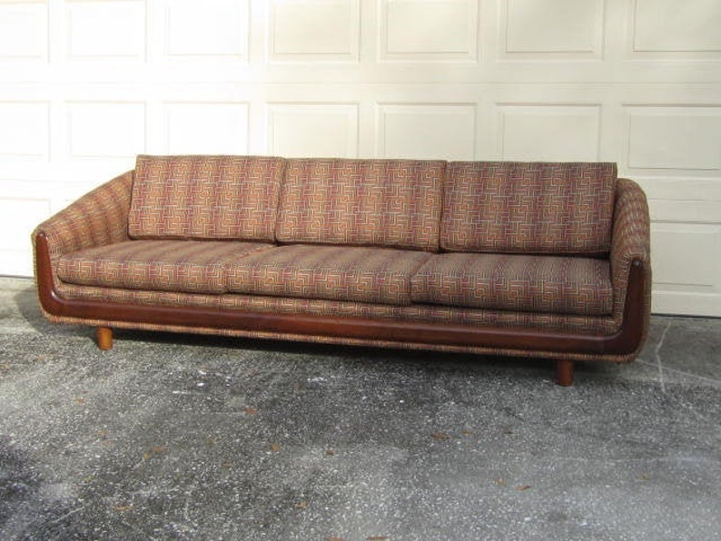 May include: A brown mid-century modern sofa with a geometric patterned fabric upholstery. The sofa has a wooden frame and legs.