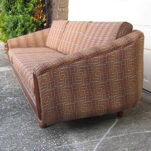 May include: A brown and orange patterned sofa with a geometric design. The sofa has a curved back and wooden legs.