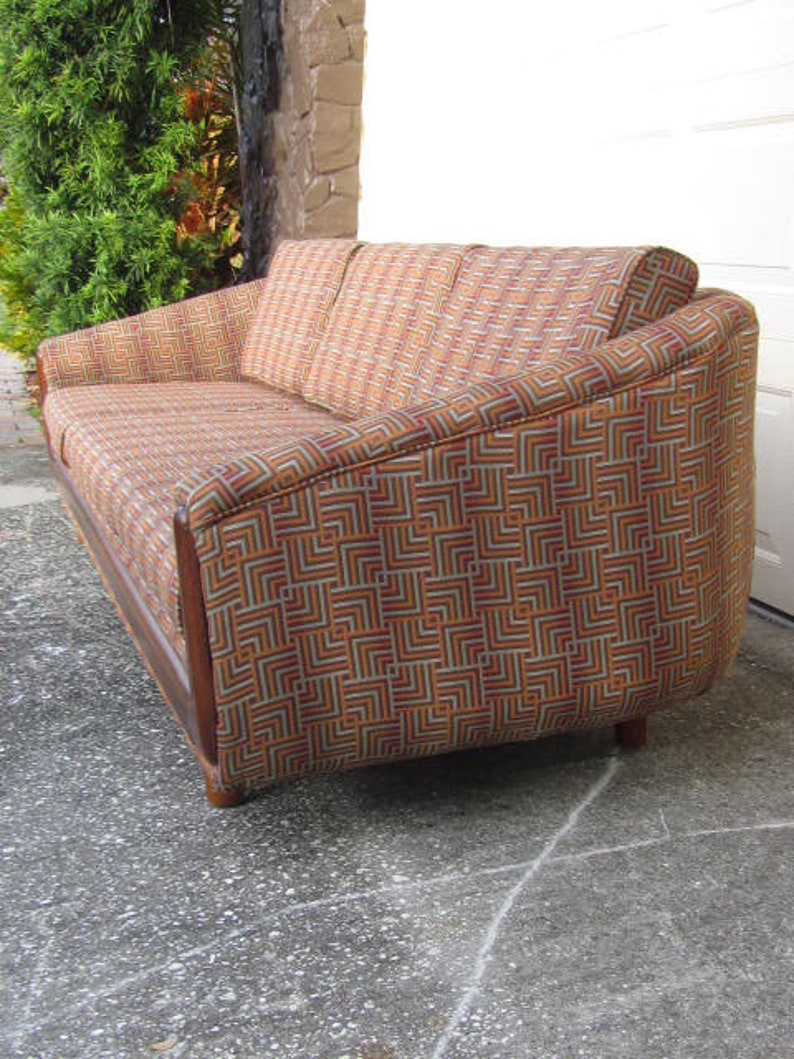 May include: A brown and orange patterned sofa with a geometric design. The sofa has a curved back and wooden legs.