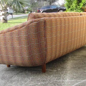 May include: A brown, orange, and white patterned sofa with a curved back and wooden legs.