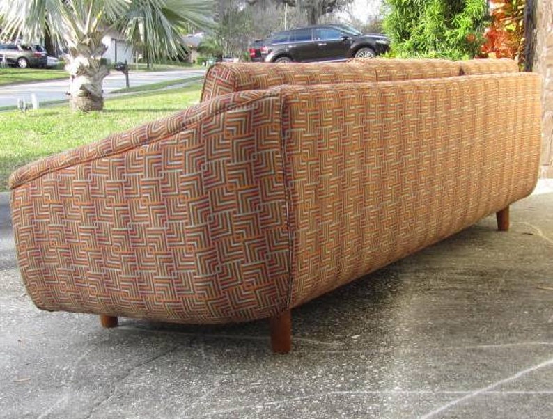 May include: A brown, orange, and white patterned sofa with a curved back and wooden legs.